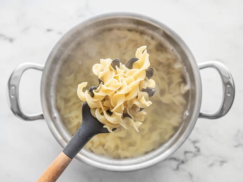 Cooked egg noodles in a pronged pasta spoon, held of the pot of water