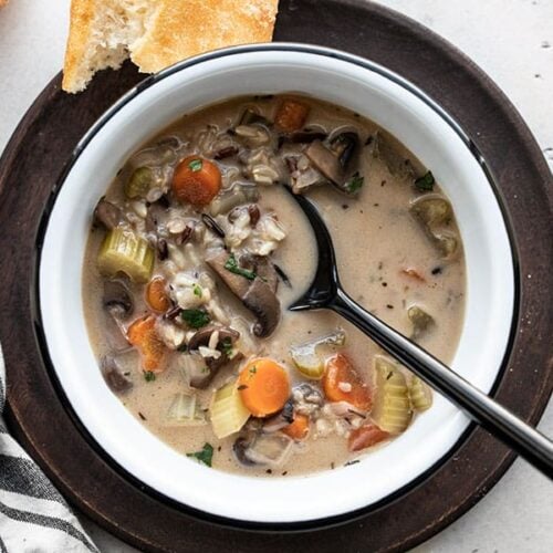 Overhead view of a bowl of Creamy vegetable wild rice soup with bread and a napkin on the side.