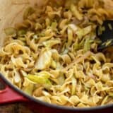 Close up of fried cabbage and noodles in a large pot, from the side