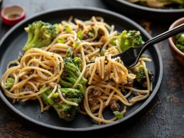 Close up of a fork twirling some Garlic Noodles with Beef and Broccoli on a black plate