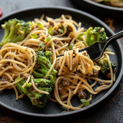 Close up of a fork twirling some Garlic Noodles with Beef and Broccoli on a black plate