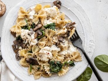 Close up of Mushroom and Spinach Pasta with Ricotta on a plate with a black fork.