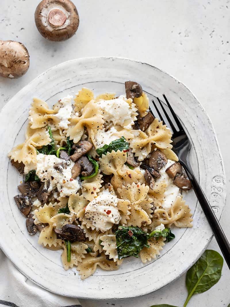 Mushroom and Spinach Pasta with Ricotta on a plate with a black fork, next to a few whole mushrooms