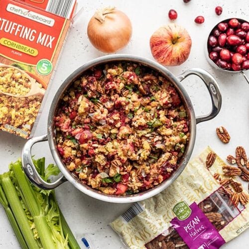 Overhead view of a pot full of Roasted Apple Cranberry Cornbread Stuffing with ingredients scattered all around