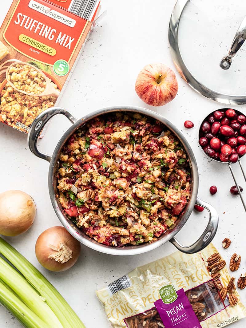 A pot full of Roasted Apple Cranberry Cornbread Stuffing with the ingredients scattered all around