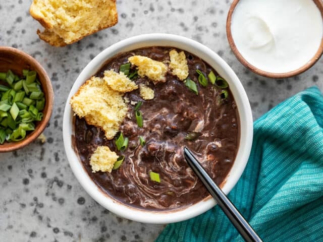 A bowl of Smoky Black Bean Soup with sour cream swirled in and a crumbled corn muffin on top
