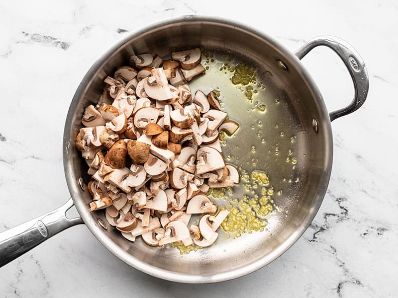 Mushrooms added to a skillet with sautéed garlic