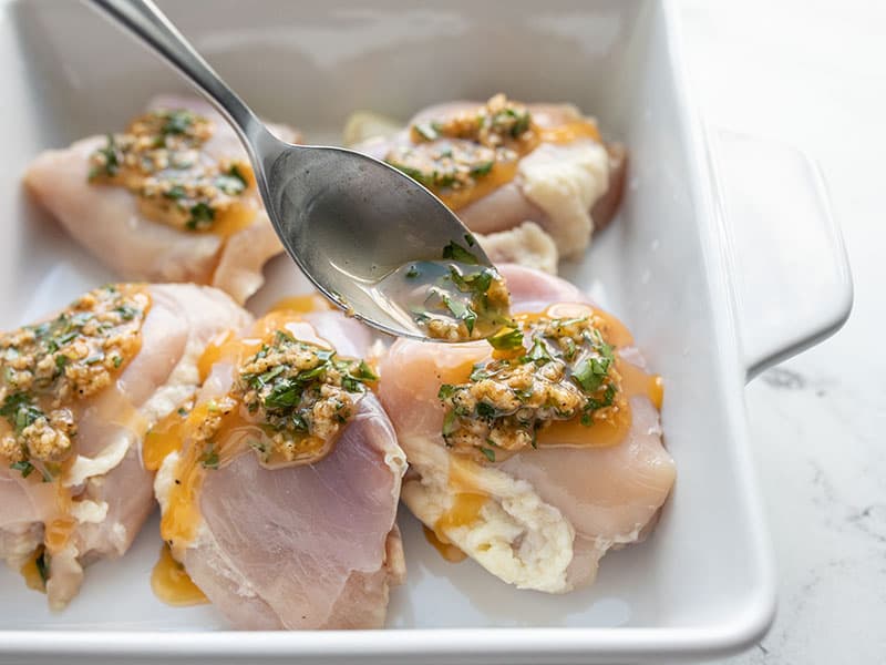 Garlic butter being spooned over chicken thighs in a baking dish
