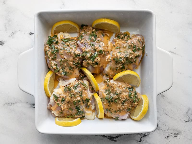 Lemon pieces added to chicken in the baking dish