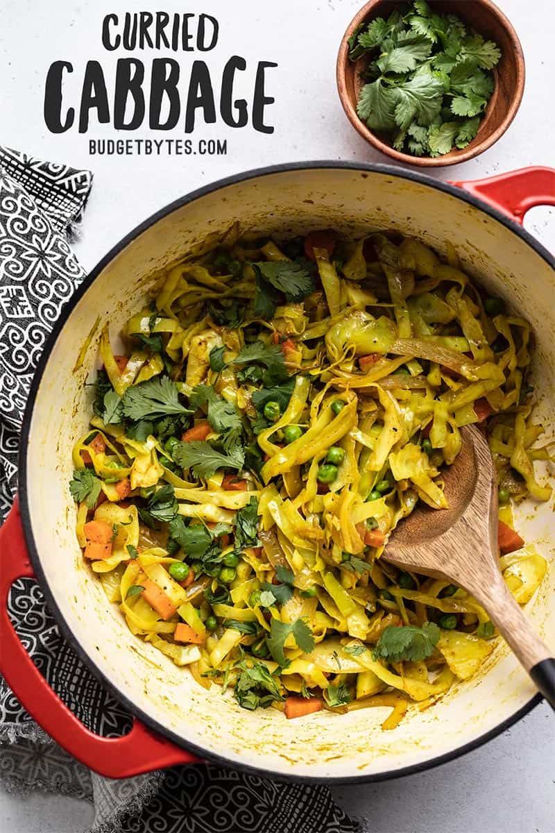 Curried cabbage in a red pot with a wooden spoon, title text overlay at the top