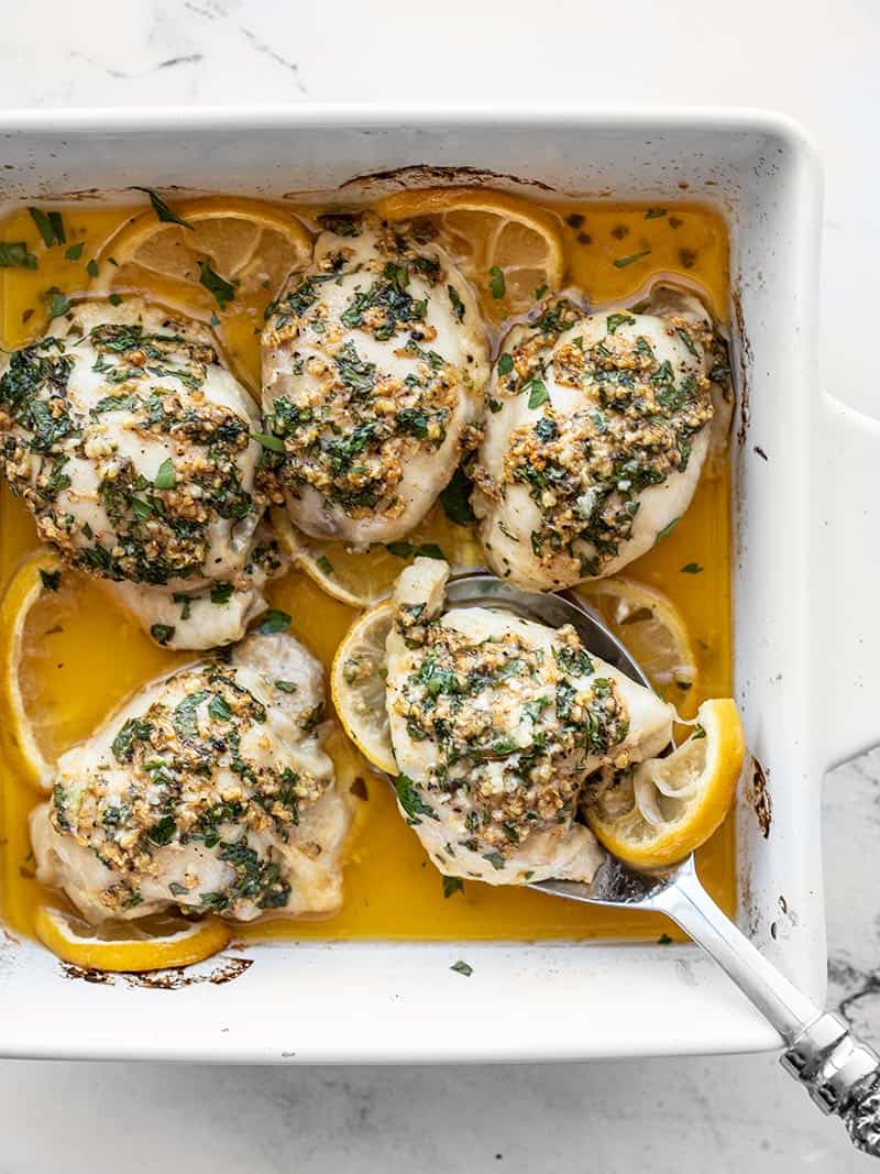 Garlic Butter Baked Chicken Thighs in a baking dish, one being scooped out with a serving spoon