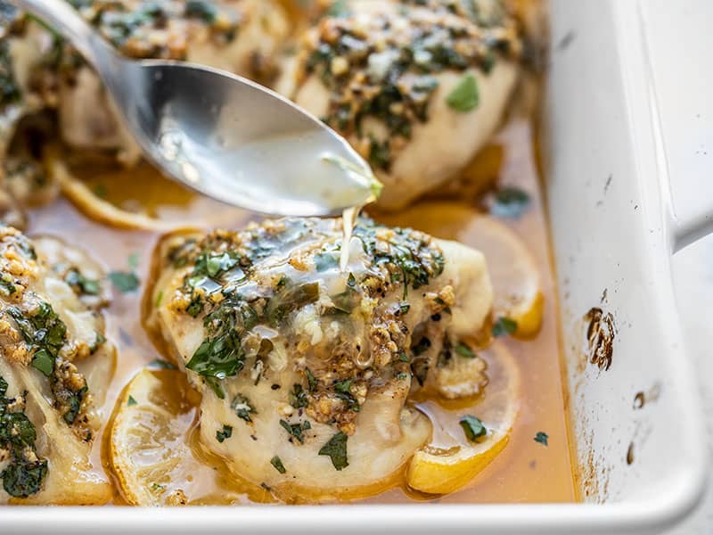 Juices being drizzled over the garlic butter baked chicken in the baking dish