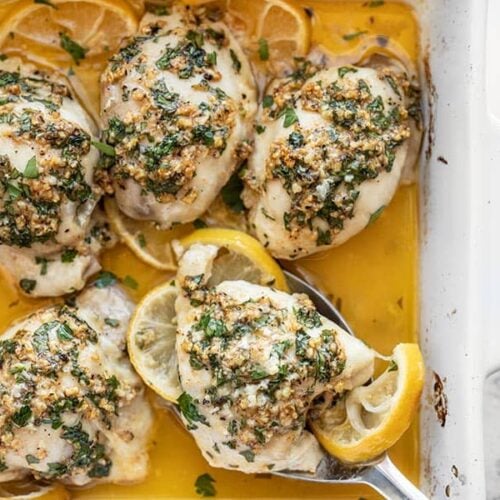 Overhead view of Garlic Butter Baked Chicken Thighs in the baking dish, one being scooped out with a serving spoon.