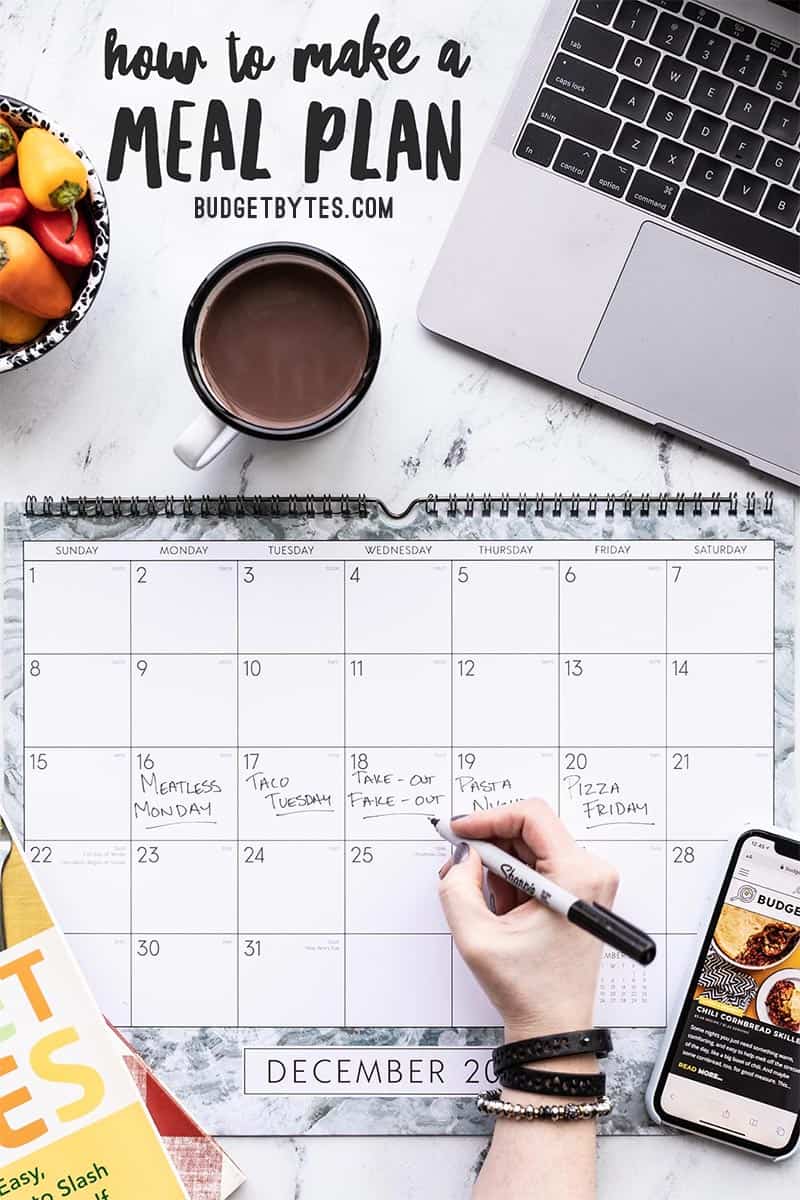 A hand writing on a calendar, surrounded by laptop, cookbooks, and iphone
