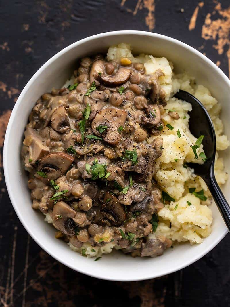 Overhead view of a bowl full of Lentils with Creamy Mushroom Gravy served over mashed potatoes, with a black spoon.