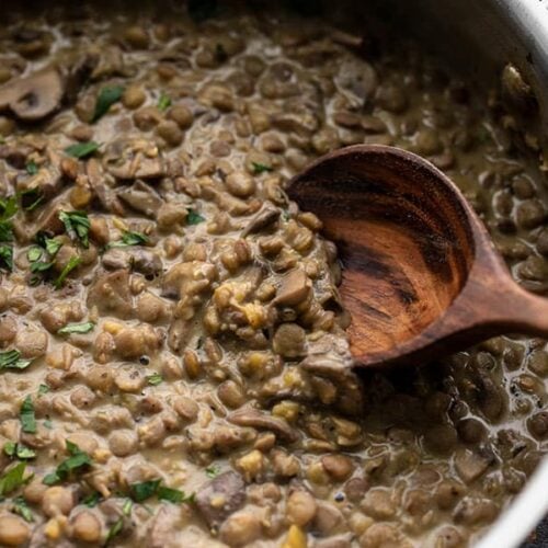 Lentils with Creamy Mushroom gravy in the skillet being scooped with a wooden spoon