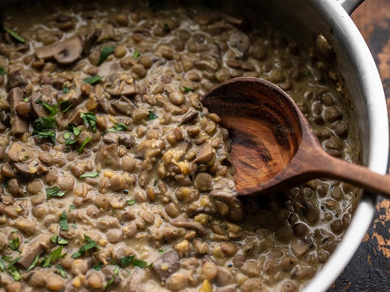 Lentils with Creamy Mushroom gravy in the skillet being scooped with a wooden spoon
