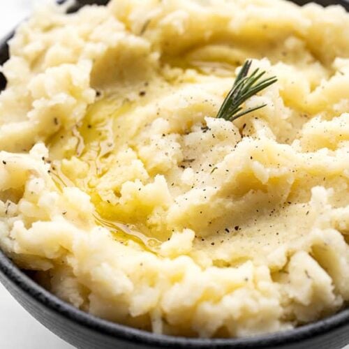 Super close up side view of a bowl of olive oil mashed potatoes garnished with rosemary and a drizzle of olive oil