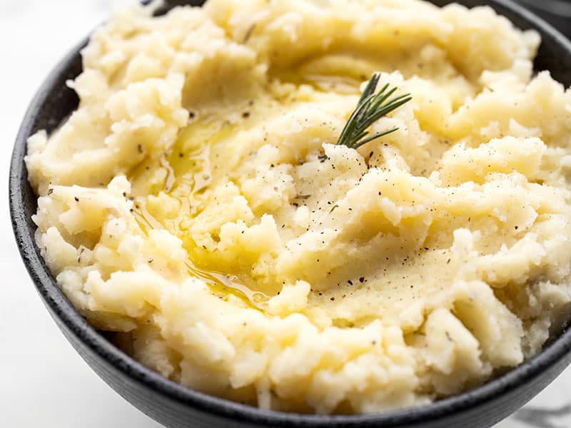 Super close up side view of a bowl of olive oil mashed potatoes garnished with rosemary and a drizzle of olive oil