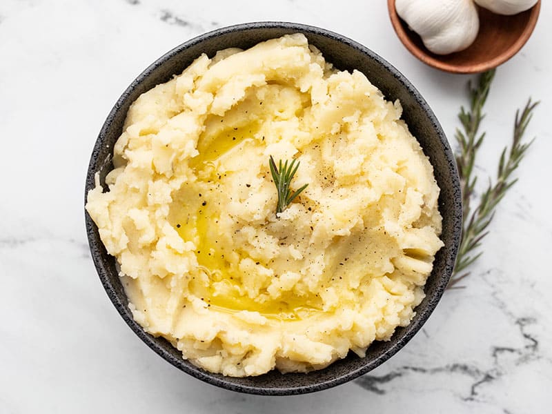 Finished bowl of Olive Oil Mashed Potatoes garnished with a drizzle of olive oil and a sprig of fresh rosemary