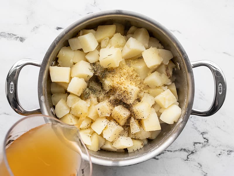 Cooked potatoes in the pot with seasoning and broth being poured in.