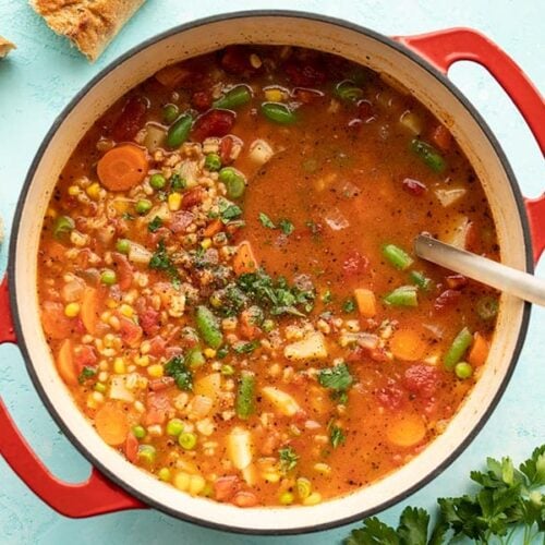 Overhead view of a pot full of vegetable barley soup with bread on the side