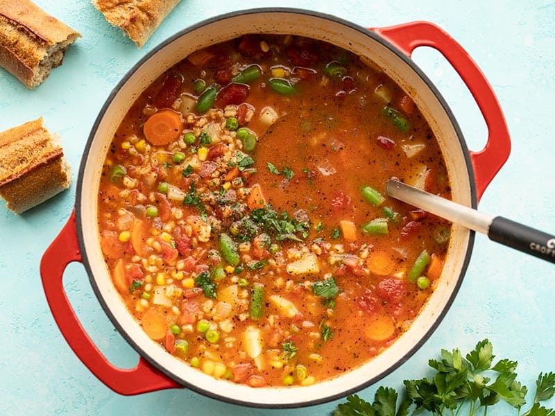 Overhead view of a pot full of vegetable barley soup with bread on the side