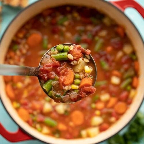 Close up of a ladle full of Vegetable Barley Soup being held over the soup pot.