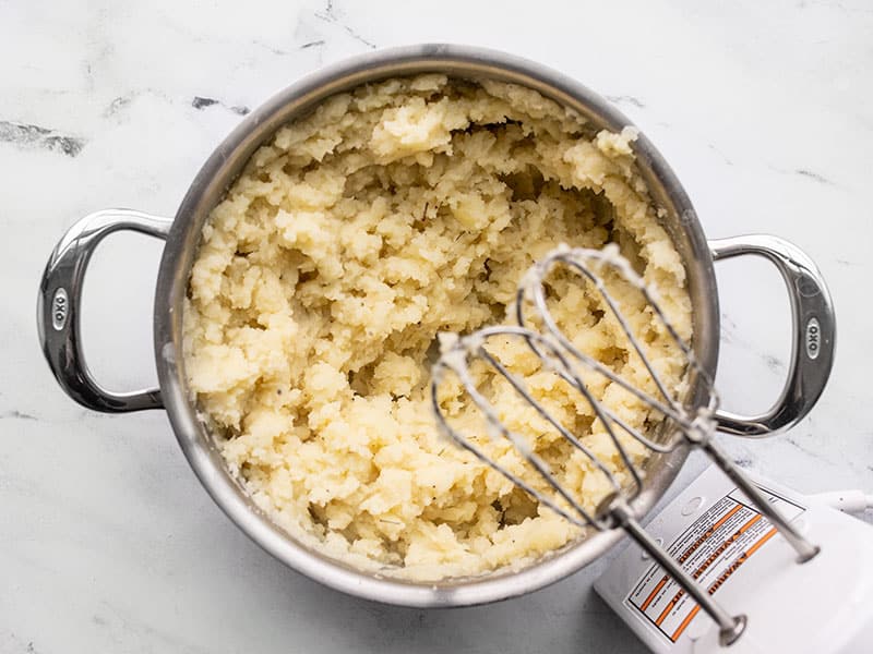 Whipped mashed potatoes in the pot with a hand mixer on the side