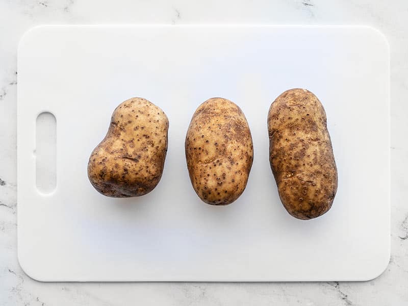 Three russet potatoes on a cutting board