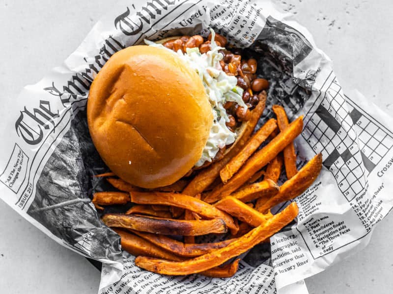 Spicy Sweet Potato Fries next to a BBQ Bean Slider in a dish lined with newsprint, viewed from above