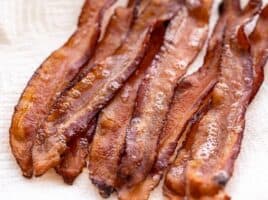 Several strips of bacon on a paper towel covered plate, viewed from the side