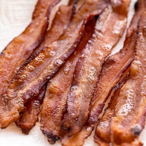 Several strips of bacon on a paper towel covered plate, viewed from the side
