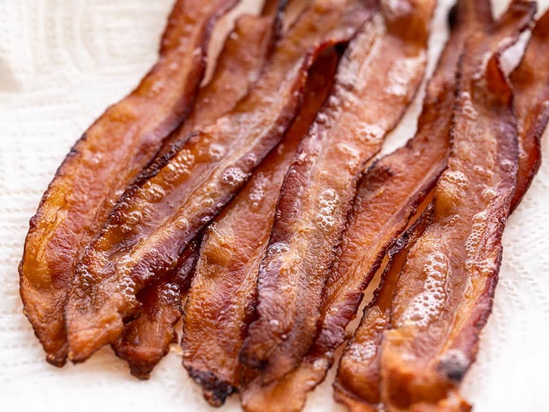 Several strips of bacon on a paper towel covered plate, viewed from the side