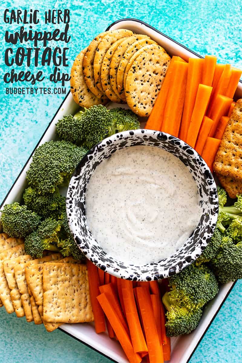 A platter of crackers and vegetables surrounding a bowl of whipped cottage cheese dip