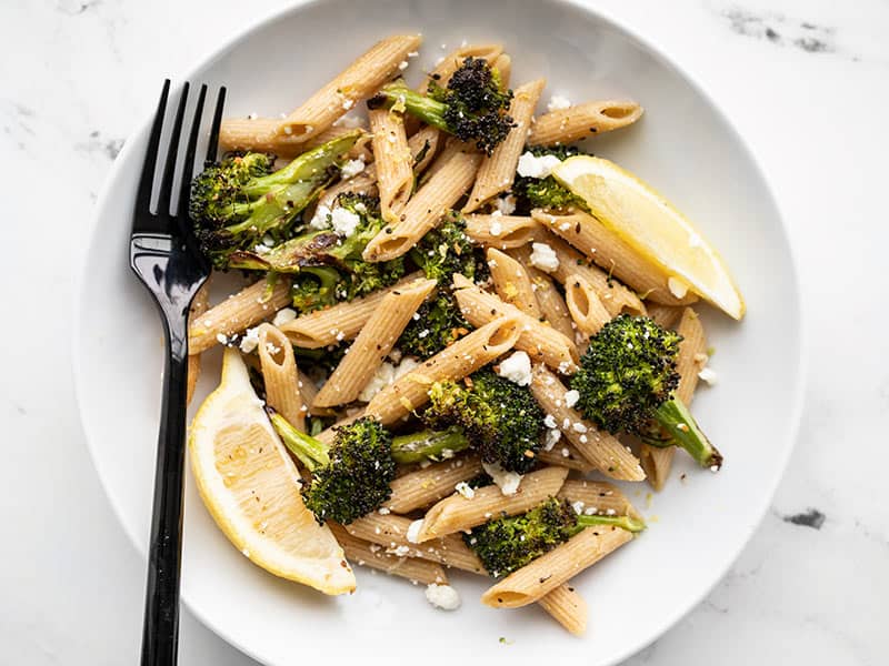 A bowl full of Roasted Broccoli Pasta with lemon and feta and a black fork on the left side