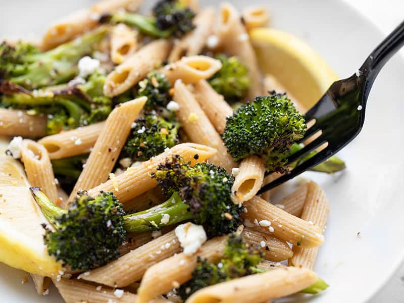 Close up view of a fork picking up some roasted broccoli pasta from the bowl