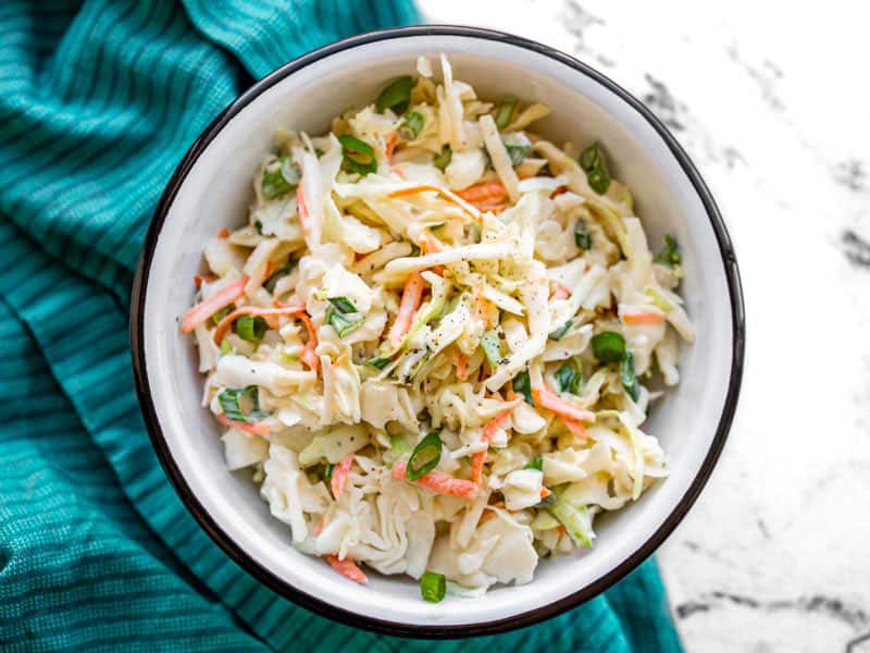 Overhead view of a bowl of creamy coleslaw on a blue napkin