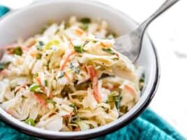 Side view of a bowl of creamy coleslaw with a fork lifting a bite