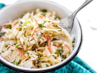 Side view of a bowl of creamy coleslaw with a fork lifting a bite