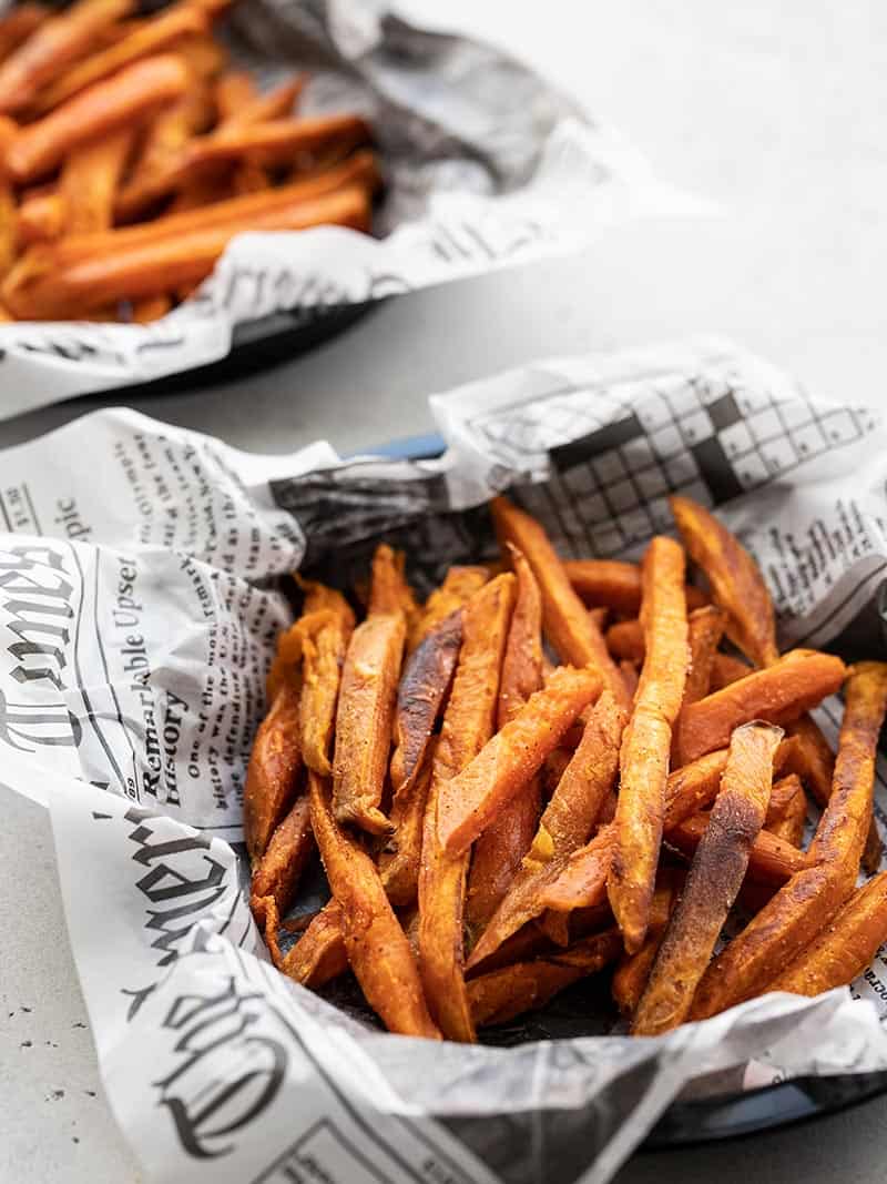 Two dishes lined with newsprint full of spicy sweet potato fries