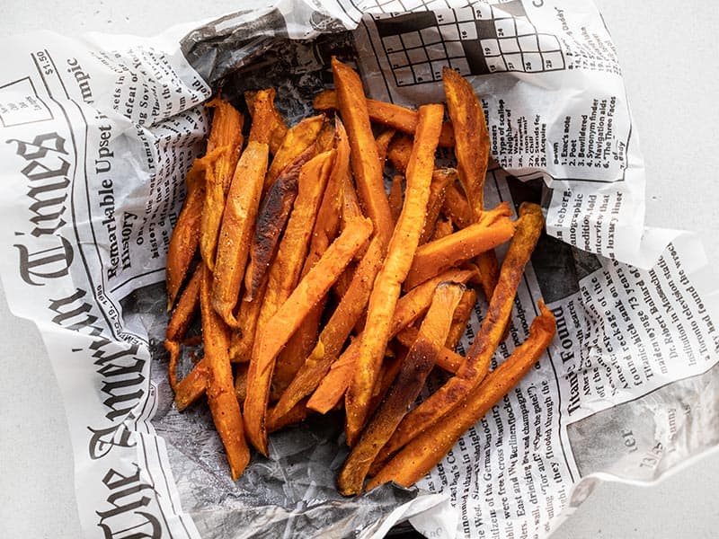 A pile of sweet potato fries in a newsprint lined dish, viewed from above