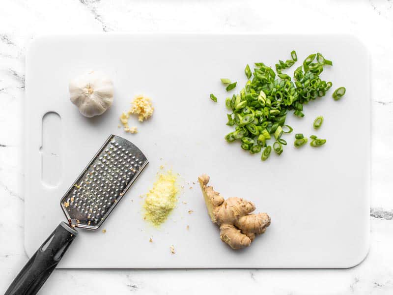 Garlic, ginger, and green onions being prepped on a cutting board