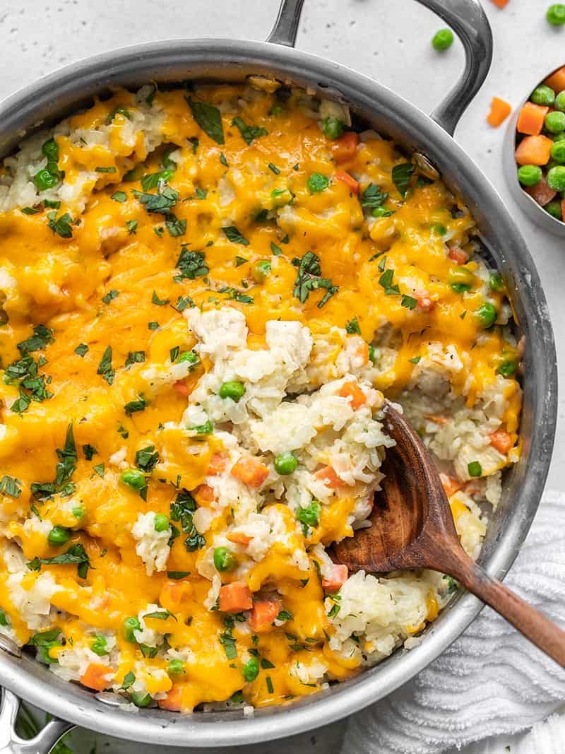 Close up of the cheesy chicken and rice skillet with a spoon scooping some of the rice.