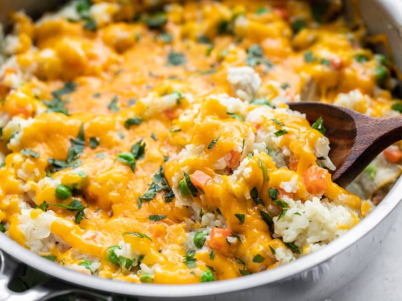 Front close up view of creamy chicken and rice skillet with a wooden spoon scooping some of the rice