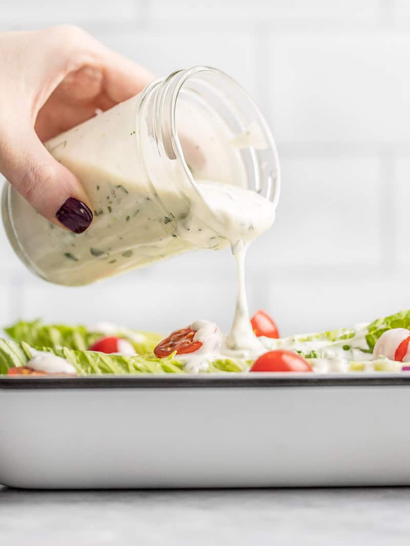Homemade ranch dressing being poured from a jar onto a salad