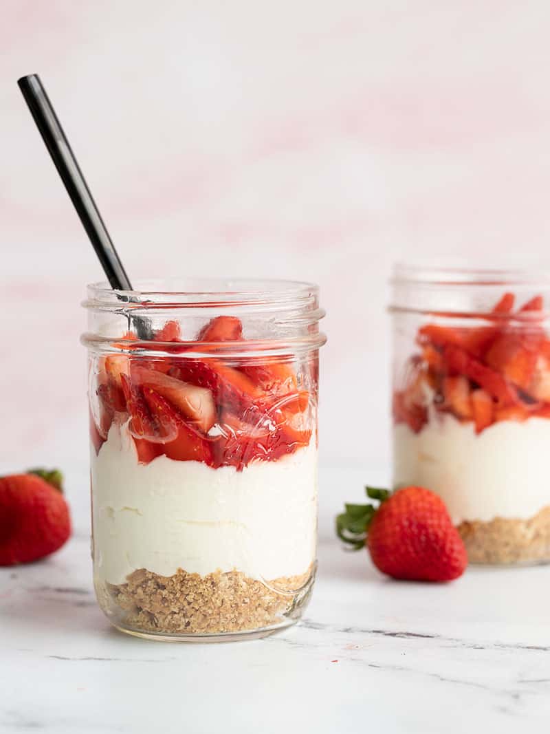 Two mason jars with no bake strawberry cheesecake, one with a black spoon