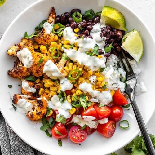 Close up overhead view of a roasted cauliflower taco bowl topped with cilantro lime ranch and a black fork in the middle