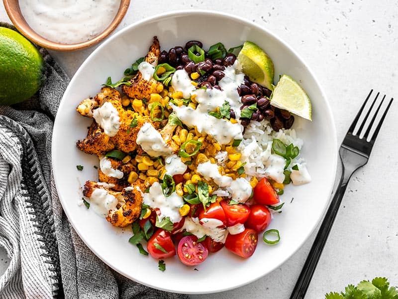 A finished roasted cauliflower taco bowl with cilantro lime ranch, with a black fork on the side.