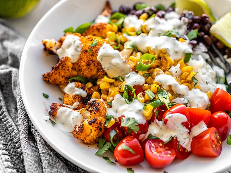 Close up side view of a roasted cauliflower taco bowl topped with cilantro lime ranch